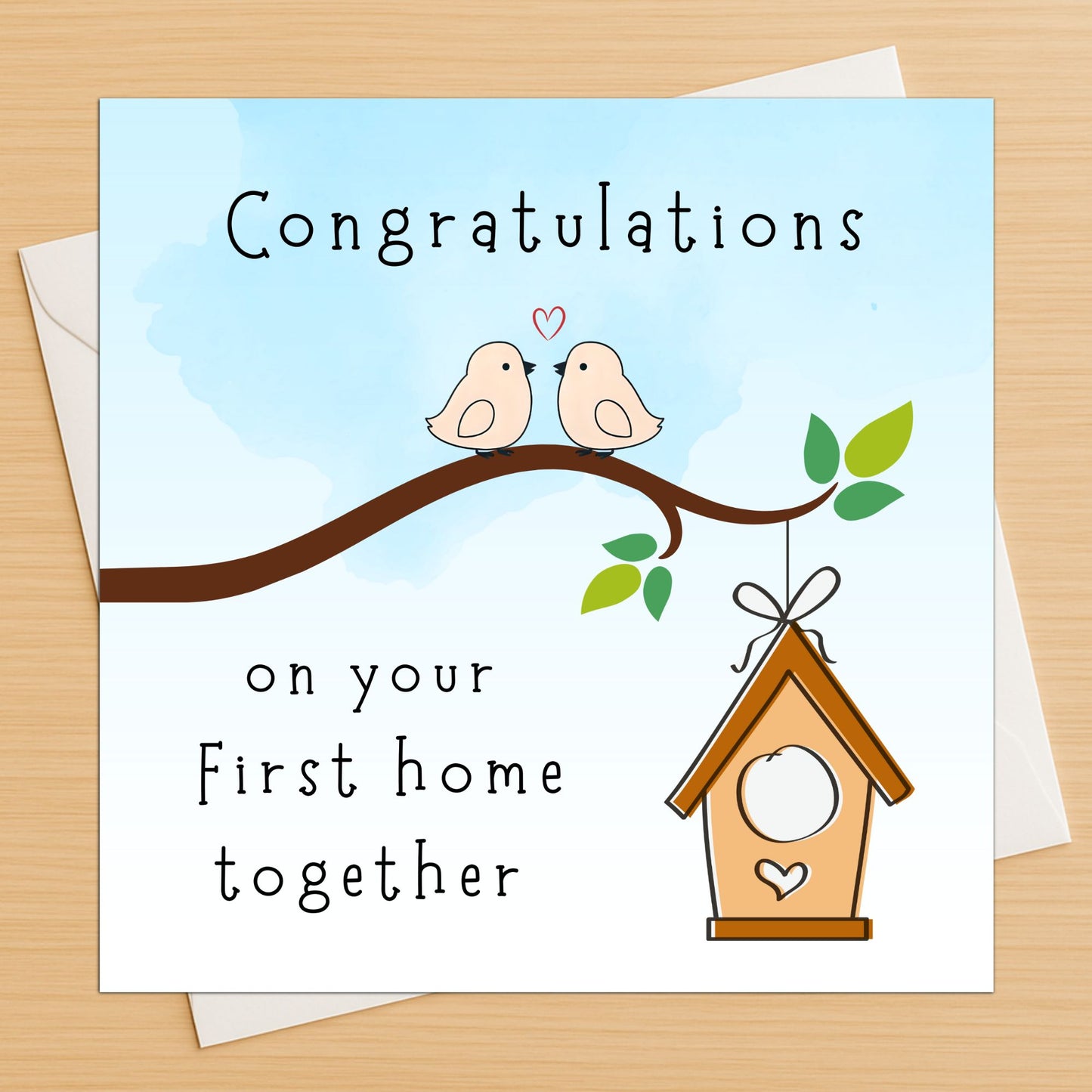 Greeting card with two birds on a branch and a birdhouse, featuring the text 'Congratulations on your First home together' on a wooden surface.