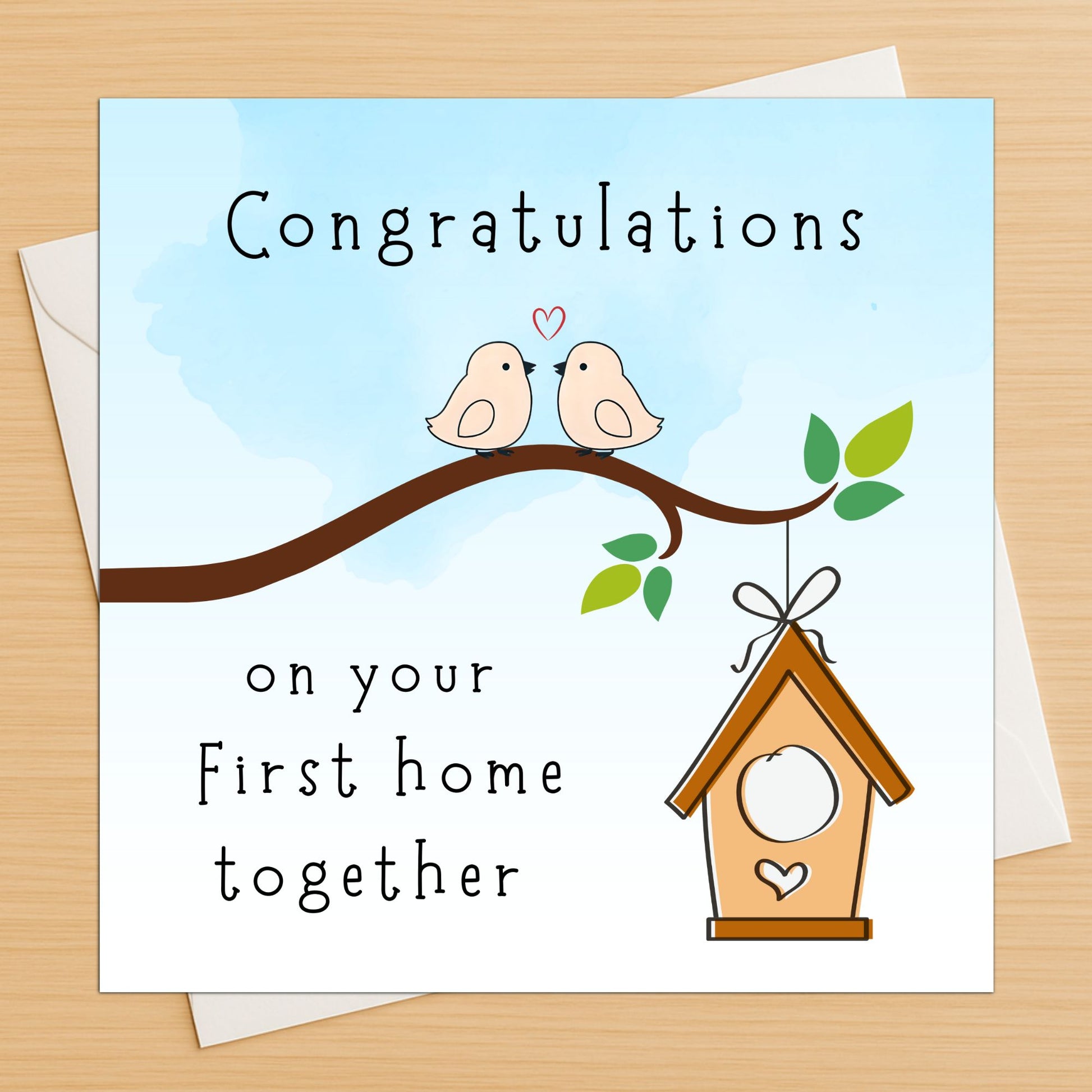 Greeting card with two birds on a branch and a birdhouse, featuring the text 'Congratulations on your First home together' on a wooden surface.