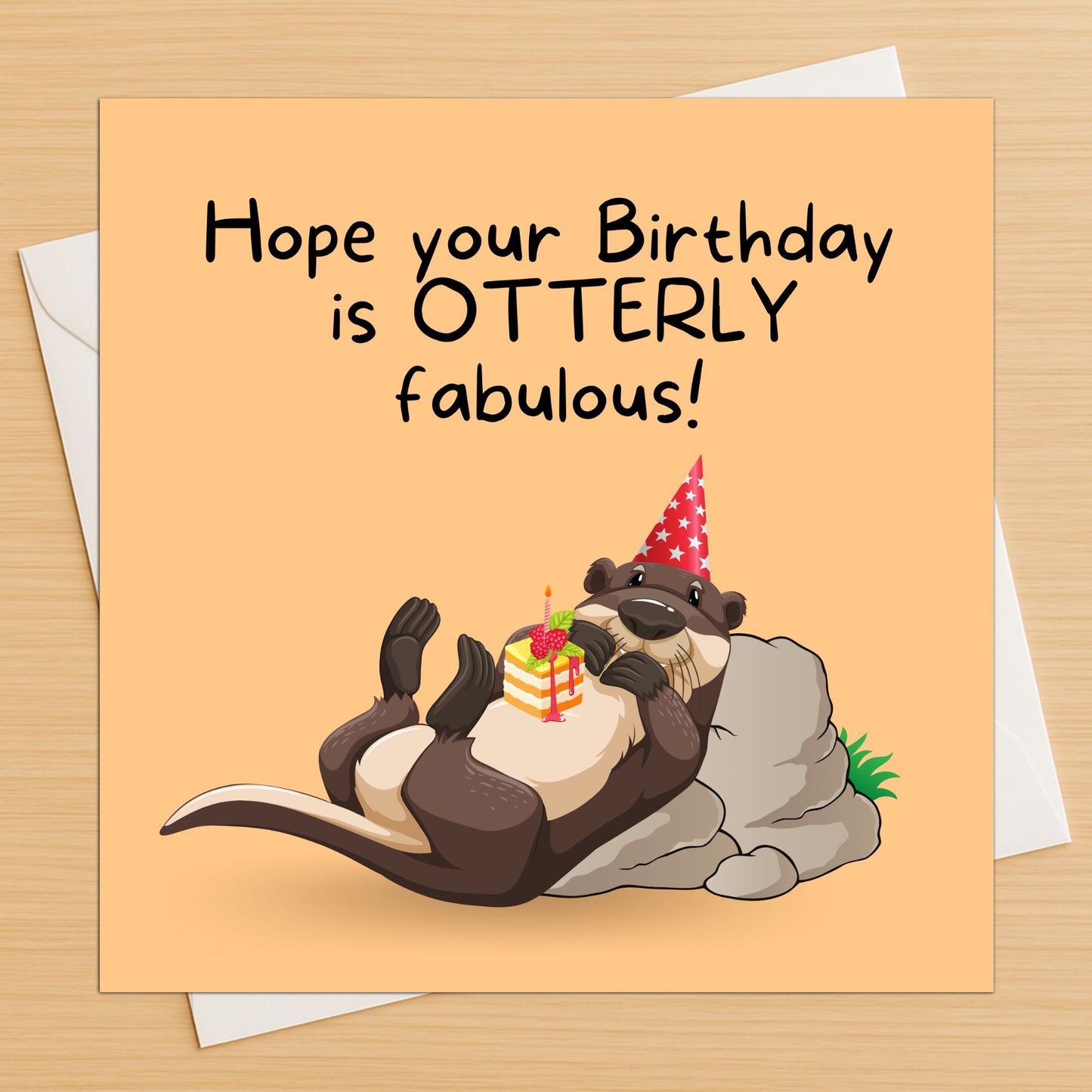 Otter pun birthday card lying flat on a wooden table with white envelope