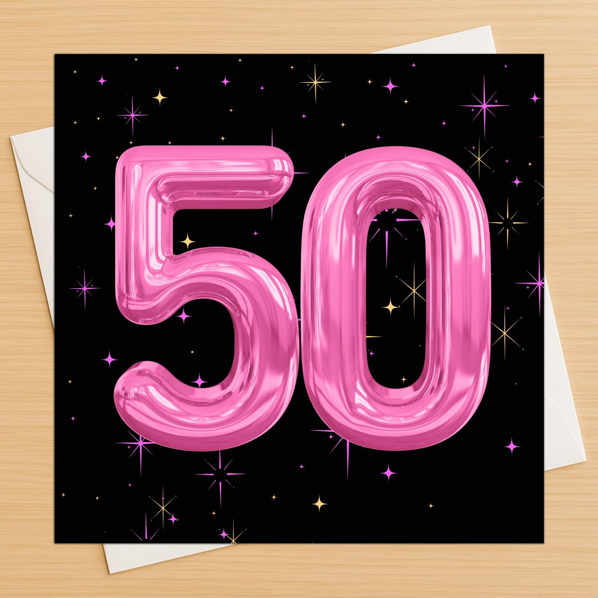 Card with pink number '50' balloons on a black background with stars, on a wooden surface.